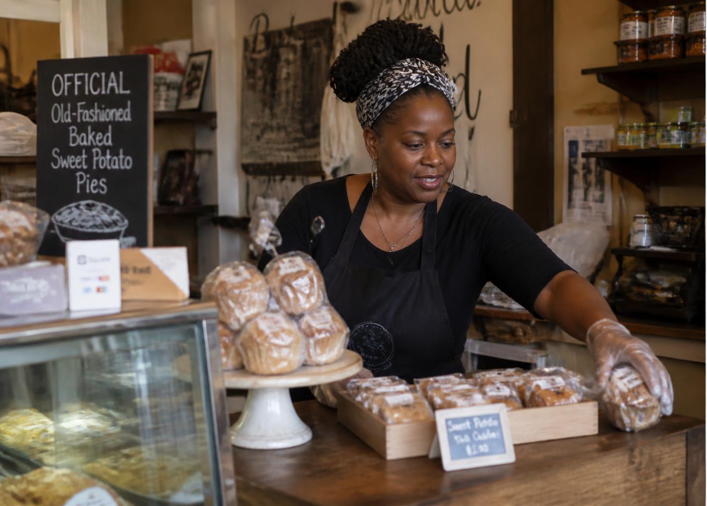 A small business owner arranging baked goods in her storefront.